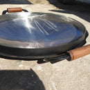 Disco de aço com borda alta e alças de madeira sobre chão de concreto ao ar livre