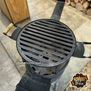 Churrasqueira portátil com grelha de ferro preto instalada sobre suporte circular em área externa