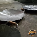 Funil de chapa com alças de madeira, dois modelos grandes em formato ondulado, sobre chão rústico