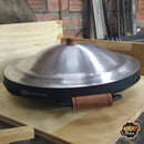 Tacho com borda e tampa de metal com pegadores de madeira em superfície de madeira